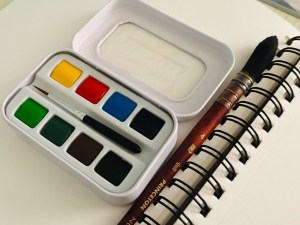 Sennelier aqua mini travel watercolor palette on a watercolor book next to a size 4 quill 