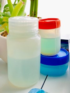 The larger Nalgene on the left, next to 2 other larger sizes of Humangear. The one on top on the right works the same as the 2 oz Nalgene, but has a wider mouth. I think they’re both 2oz. There’s a plant on the desk in the background. 