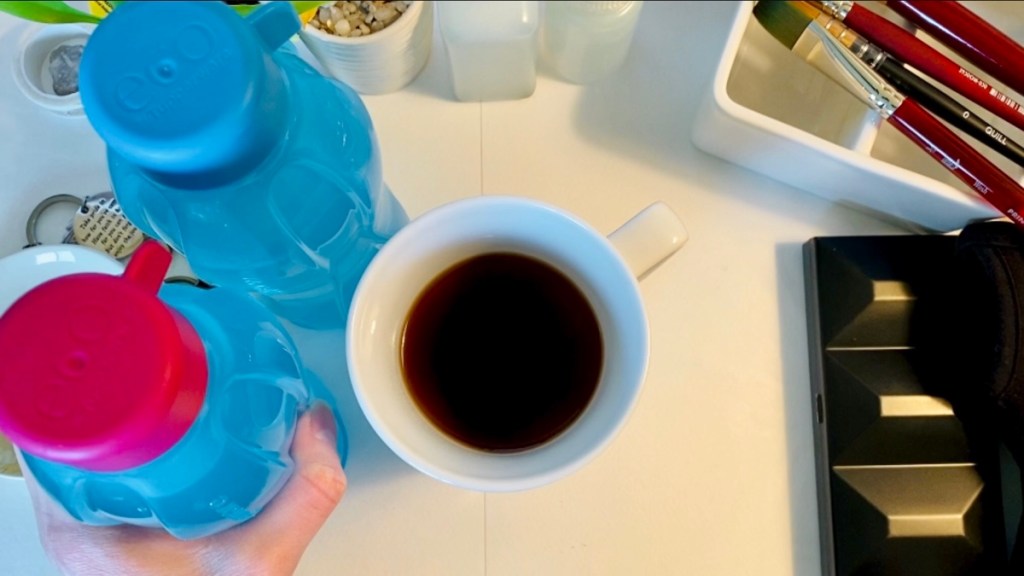 Tupperware eco water bottles, at the desk from a top down view, there’s a paint palette and a few brushes to the right, and one of the water bottles has a pink cap on a blue bottle