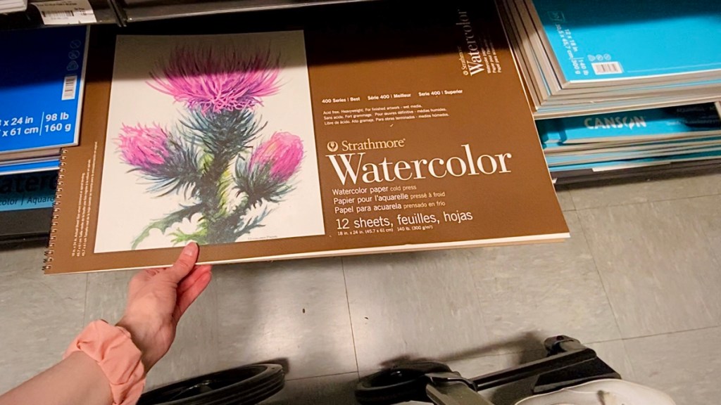 My hand holding the giant Strathmore 400 18x24 watercolor paper in Blick art materials in DC