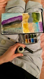 watercolor mountain in my lap on my watercolor book, and the facing page is watercolor swatching of those colors 